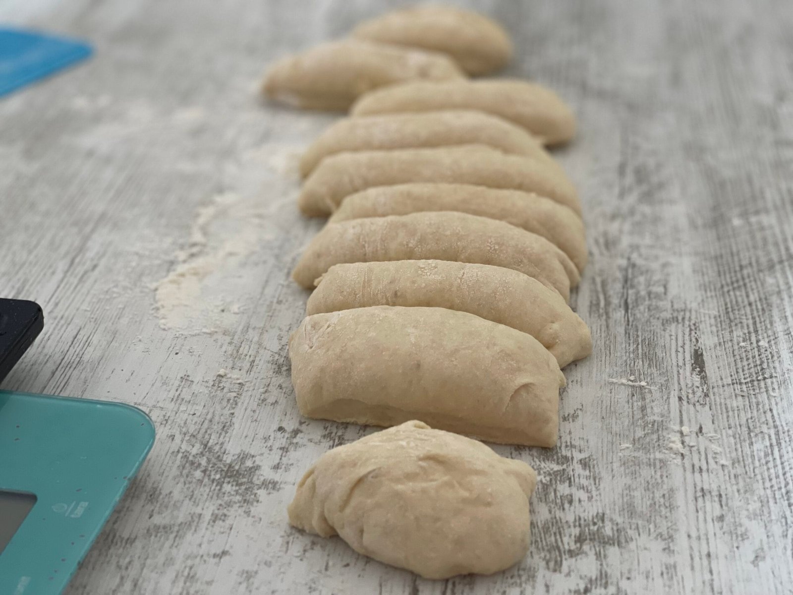 Aluat împărțit în porții egale pe blat, pregătit pentru modelarea chiflelor de casă pentru hot dog
