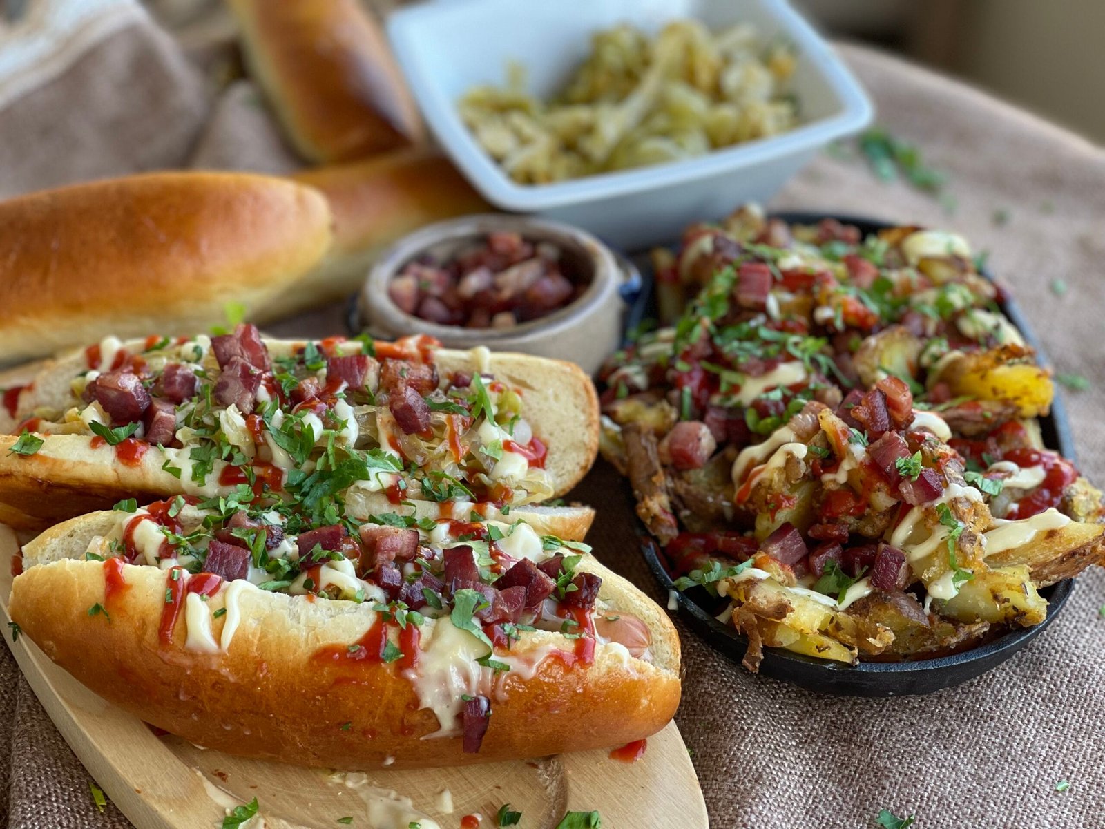 Imagine detaliată cu hot dog asamblat, evidențiind stratul de varză murată, ceapă caramelizată, bacon crocant și sosuri în chiflă de casă