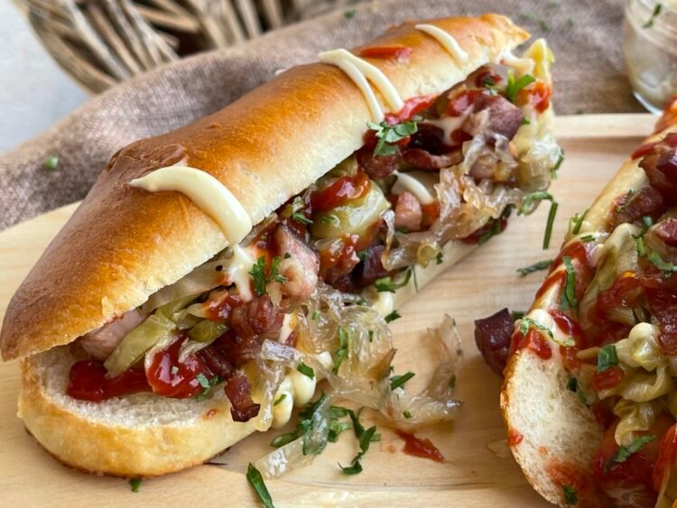 hot-dog-rasturnat-close-up Hot dog răsturnat pe o parte, arătând detalii cu varză murată, ceapă caramelizată, bacon crocant și sosuri în chiflă pufoasă de casă