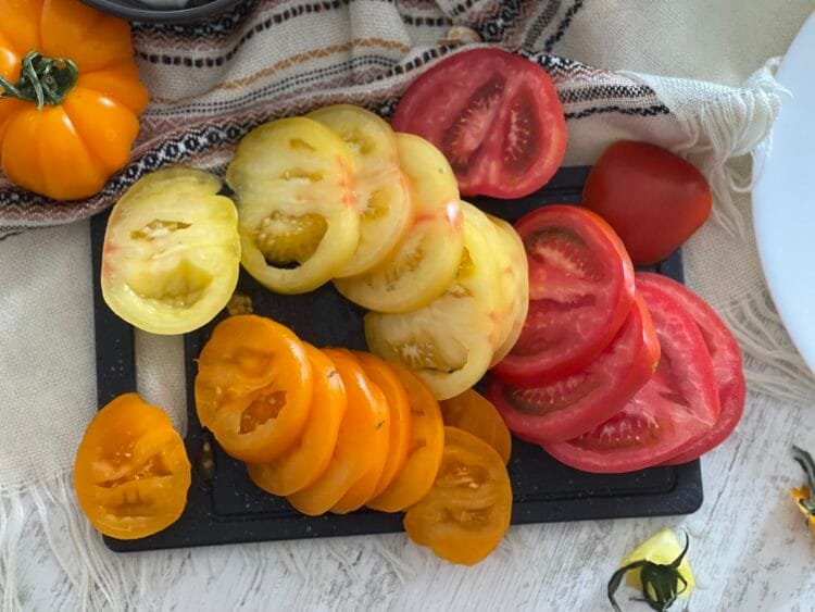 Felii de roșii colorate (roșii, galbene, portocalii) așezate pe tocator, pregătite pentru galette.