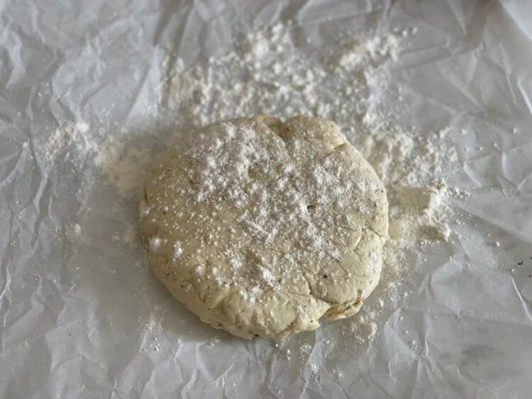 Bilă de aluat pe hârtie de copt, presărată ușor cu făină, pregătită pentru a fi întinsă în vederea pregătirii unei galette rustice.
