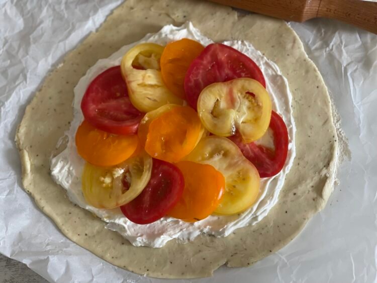 galette-rosii-colorate-peste-crema Feliile de roșii variate ca formă și culoare așezate peste crema de brânză pe aluat, înainte de împachetarea marginilor galettei.