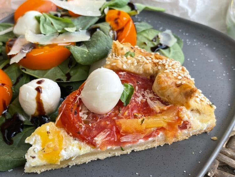 Close-up cu o felie de galette rustică cu roșii, așezată pe farfurie lângă salată verde proaspătă.