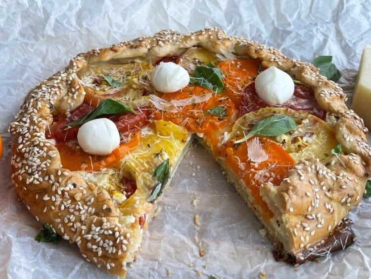 Tartă rustică galette cu roșii, fotografiată de aproape, cu o felie lipsă și interiorul bine vizibil – aluat fraged, cremă de brânză și roșii colorate, așezate artistic.